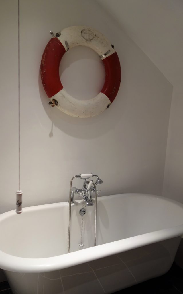 A white roll top bathtub with a red and white lifebelt on the wall above.